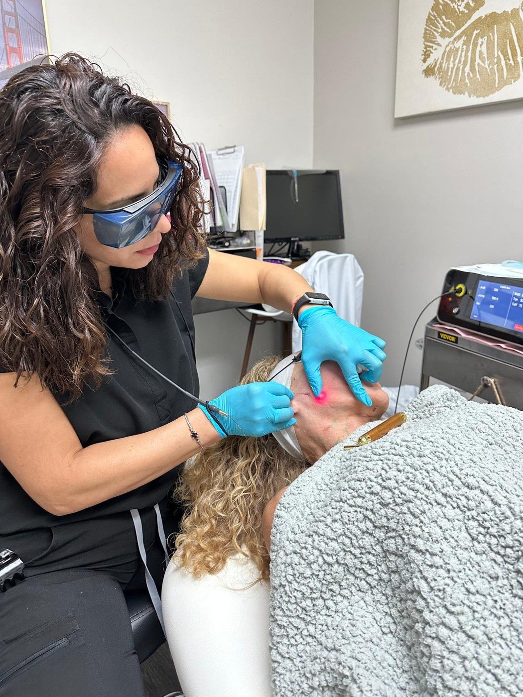 A provider in protective glasses treats a patient's face with a laser