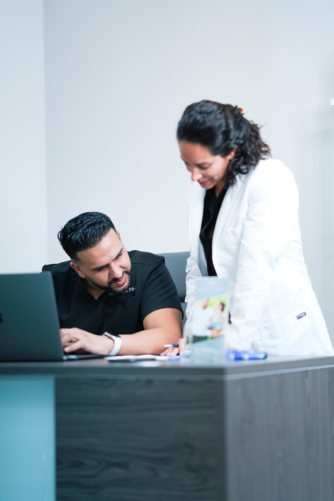 Two colleagues review something on a laptop at a front desk